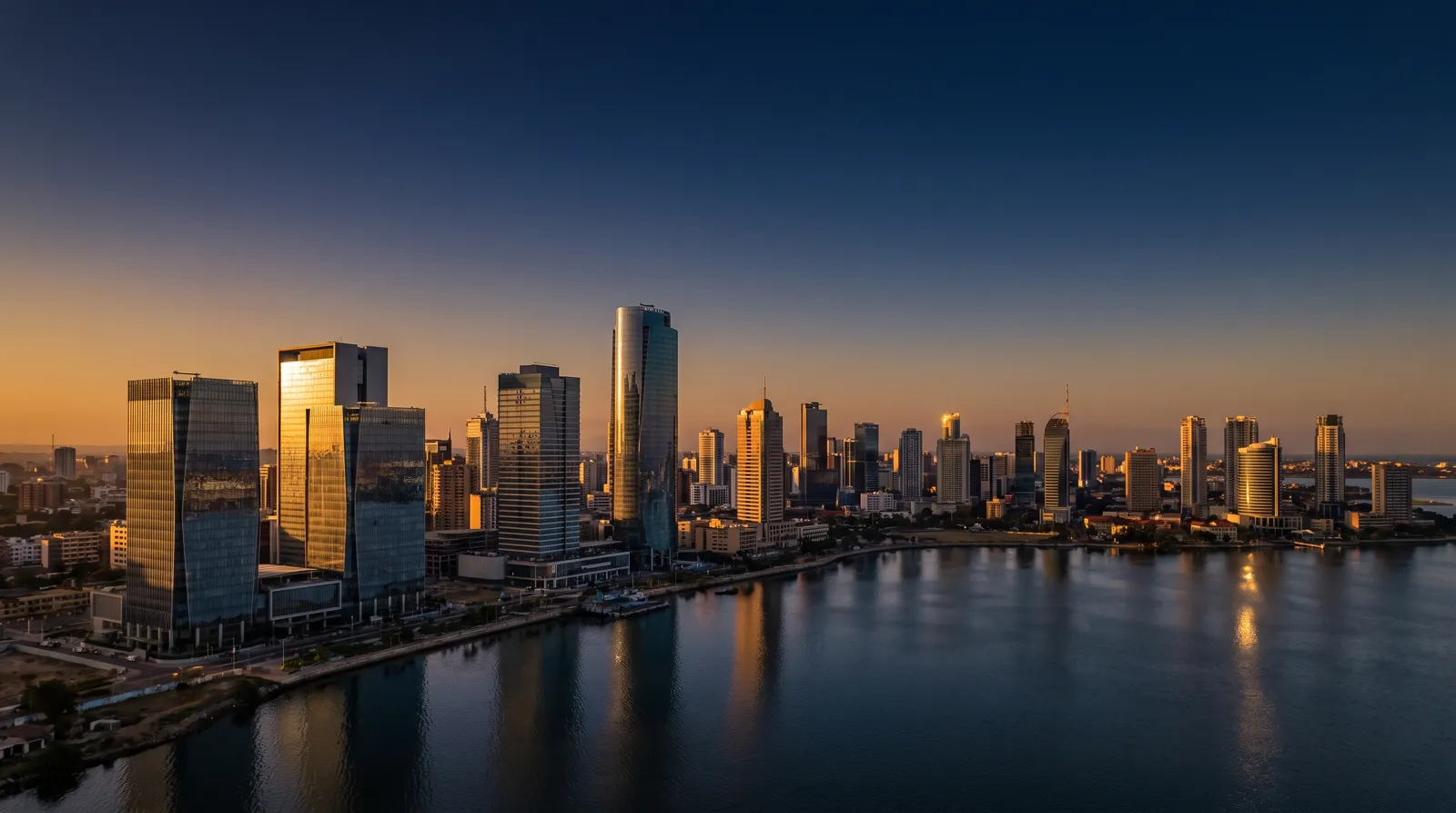 A modern African business district of glass towers across the water at golden hour